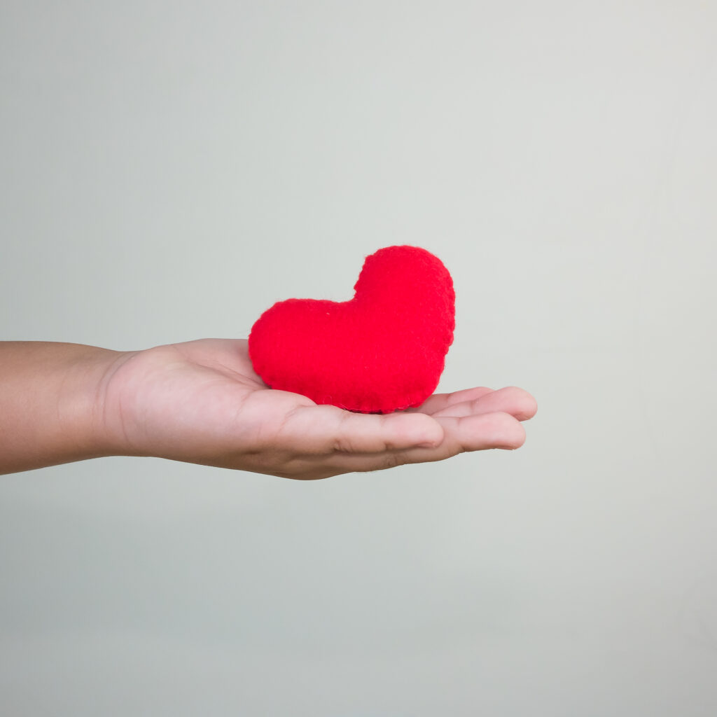 close up hand holding red heart shape against gray background